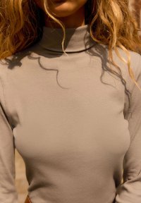 Jasno beżowy prążkowany golf o dopasowanym kroju. Tkanina ma gładką fakturę, podkreślającą kontury. Długie rękawy z minimalnymi detalami.