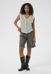 Knitted sleeveless top with black stripes on a cream background, paired with gray denim shorts and black knee-high boots.