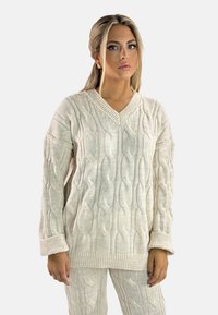 Cremfarbener Kabelstrickpullover mit V-Ausschnitt, langen Ärmeln und lockerer Passform. Merkmale sind markante strukturierte Muster und gerippte Saumdetails.