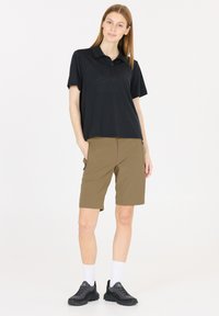 Svart pikétröja med krage och två knappar, ihop med tanfärgade shorts med sidofickor. Bärs med svarta löparskor och vita strumpor.