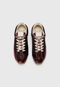 Sneaker borgogna con pannelli in suede neri, lacci crema e cuciture a contrasto. Caratterizzano una punta in pelle liscia e accenti laterali testurizzati.