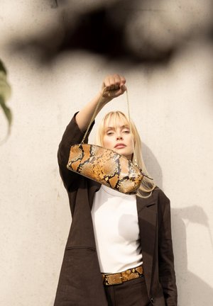 Snake-print clutch bag with a curved shape, golden chain strap, and a beige and black color palette, held by a person wearing a brown blazer.