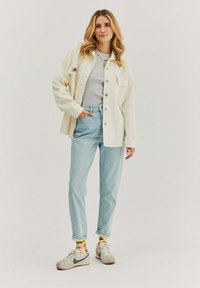 Krémová oversize košile s kapsami, šedý fitted top, světle modré rovné džíny a tenisky s vzorovanými žlutými ponožkami.