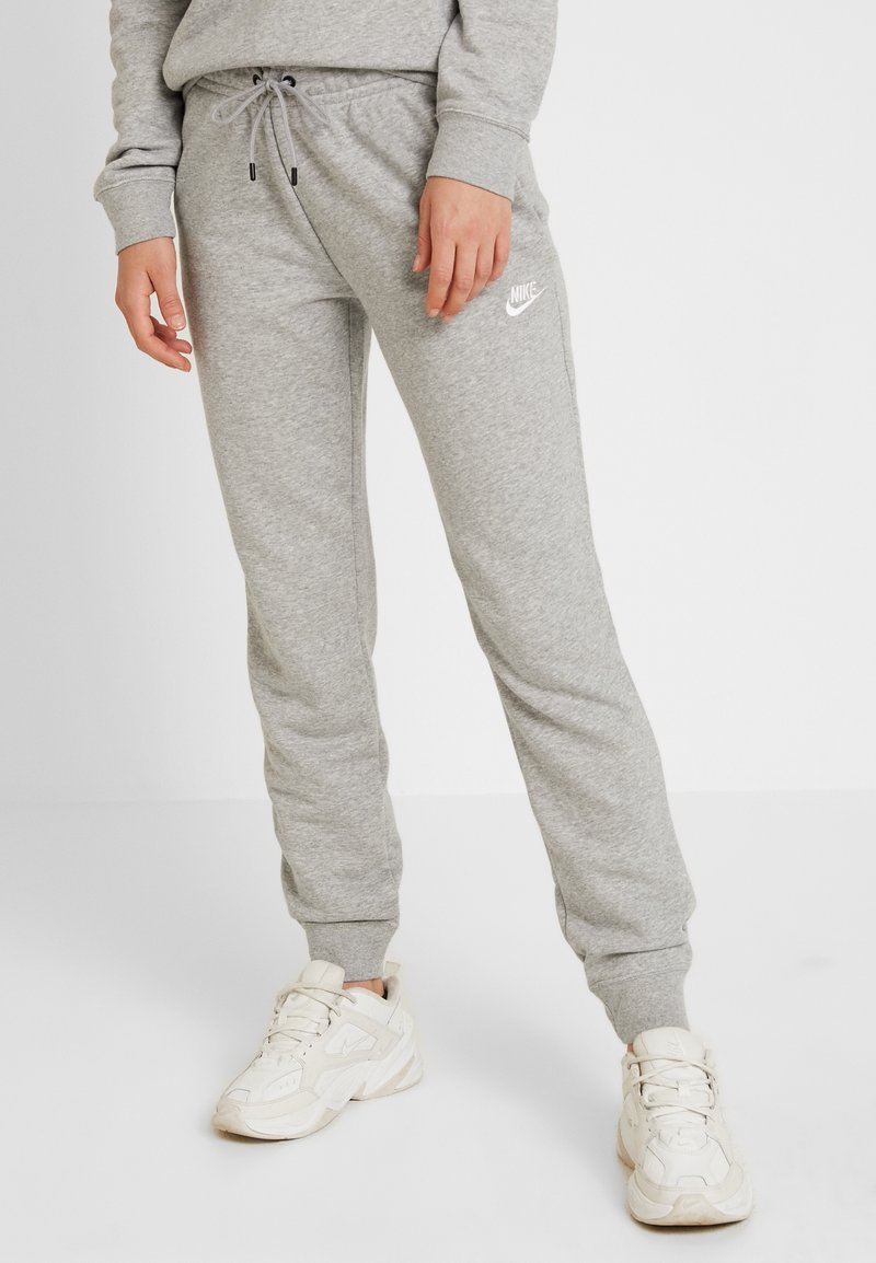 Grey cotton sweatpants with drawstring waist, tapered legs, and a white Nike logo on the left thigh. Paired with white athletic shoes.