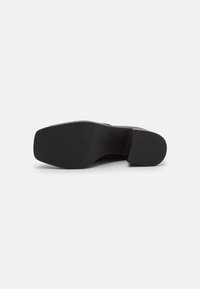 Sort sko med en flad, struktureret sål og en let hævet hæl. Designet er minimalistisk med en glat overflade og afrundede kanter.