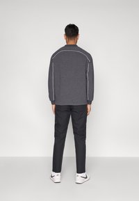 Γκρι φούτερ με άσπρες ραφές, συνδυασμένο με μαύρο παντελόνι και λευκά αθλητικά, απεικονίζεται από πίσω, με απλό σχέδιο.