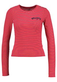 Röd långärmad tröja med vita horisontella ränder. Har en rundad halsringning och "Hollister"-logotyp i marinblått på bröstet. Tillverkad av mjukt tyg.