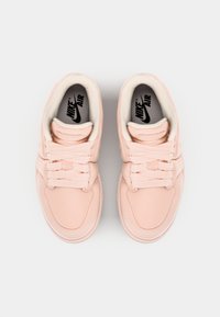 Nike Air sneakers in soft pink synthetic material, featuring a smooth texture, rounded toe, and flat laces. Brand logo visible inside.