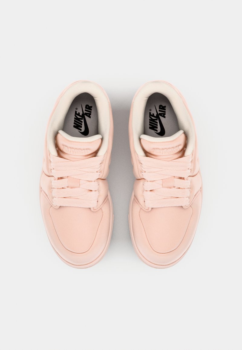Zapatillas Nike Air en suave material sintético rosa, con una textura lisa, puntera redondeada y cordones planos. Logo de la marca visible en el interior.
