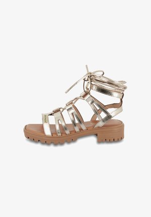 Sandales gladiateur dorées métalliques avec une semelle plate et texturée, comprenant plusieurs lanières et un laçage au niveau de la cheville.