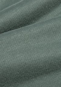 Tissu doux plié avec une texture en tricot serré de couleur bleu-vert atténuée, montrant des détails fins du fil et des ombres subtiles.