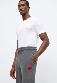 Λευκό βαμβακερό μπλουζάκι με κόκκινο λογότυπο "HUGO", συνδυασμένο με γκρι παντελόνια φόρμας από φλις που διαθέτουν κόκκινο διακριτικό λογότυπο στην αριστερή τσέπη.