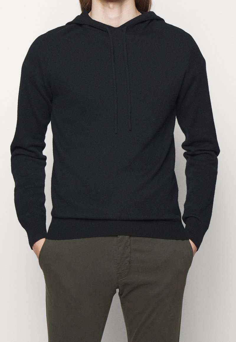 Zwarte hoodie met een zachte textuur, lange mouwen en een trekkoord. Gepaarde met olijfgroene broek, met een slim fit.