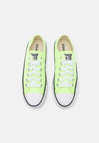 Un paio di sneakers Converse low-top di colore verde neon con lacci e punte bianche, viste dall'alto su uno sfondo bianco.