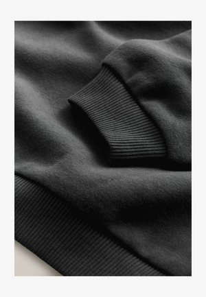 Čierna mikina s hladkou textúrou látky a rebrovanými manžetami, so záberom zblízka na detail rukáva.