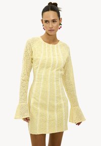 Vestido amarillo de encaje con mangas largas y acampanadas y patrones de ojal. Silueta ajustada con rayas verticales y escote redondo.