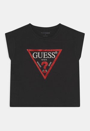 T-shirt court noir avec un logo triangulaire métallique rouge présentant "GUESS U.S.A." et un point d'interrogation au centre.