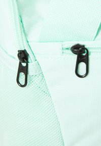 Mochila de tejido verde menta con cremalleras negras, detalles de malla y una superficie texturizada. Las cremalleras tienen tiradores de metal duraderos para un acceso fácil.