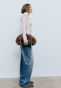 Braune Fell-Handtasche mit einer goldenen Kettenriemen, kombiniert mit einem weißen Spitzenoberteil mit langen Ärmeln und weit geschnittenen Jeans. Glatte Texturen und kontrastierende Farben.