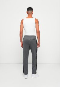 Grå sportbukser med tapered ben, elastisk talje og sidelommer. Har sorte sidelæg med logo tekst. Bæres med en hvid tanktop.