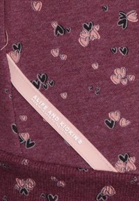 Tessuto color mogano con motivi a cuore rosa e neri sparsi, caratterizzato da un'etichetta rosa con il testo "ALIFE AND KICKIN®". Texture morbida.