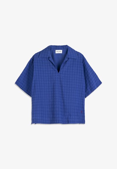Chemise à manches courtes bleue avec un motif discret en quadrillage, col ouvert et un petit détail brodé rouge près de l'ourlet.