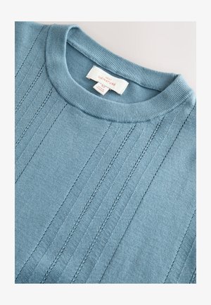 Pull en tricot bleu clair avec un col rond, présentant des détails côtelés verticaux et une étiquette en tissu indiquant la taille M.
