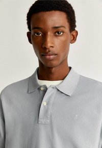 Grijze polo met een textuurstof, voorzien van een klassieke kraag, een knoopsluiting met drie knopen en een klein logo op de linkerkant van de borst.