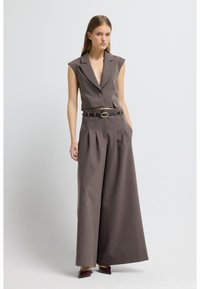 Šedý overal bez rukávů s přiléhavým živůtkem, širokými nohavicemi, záhyby a páskem. Má výstřih s výřezem a zapínání na jeden knoflík.