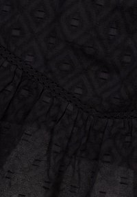 Tissu noir texturé présentant un motif en diamant avec des accents en relief et un bord froncé. Détail en dentelle délicate le long de la couture.