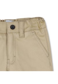Pantalons en coton beige avec une taille élastique, une fermeture à bouton noir et deux poches avant ; présentent des coutures diagonales et une texture douce.
