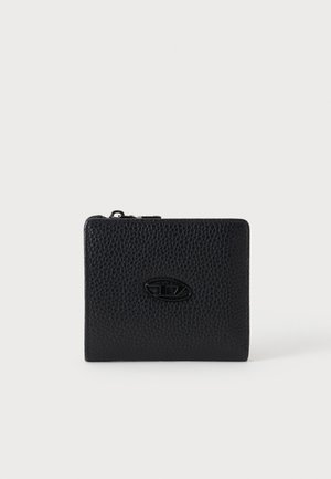 Portefeuille en cuir noir texturé avec fermeture éclair et petit badge ovale en métal avec logo au centre sur fond neutre.