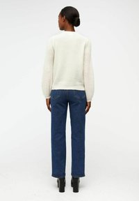 Pull crème clair avec des manches texturées, associé à un jean bleu droit et des bottes à talons carrés noires, vu de dos.