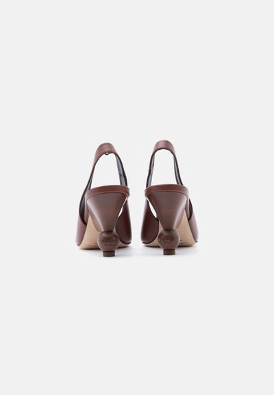 Καφέ δερμάτινα πέδιλα με λουράκι στο πίσω μέρος και στρογγυλεμένες, γλυπτικές, χοντρές τακούνια, εμφανιζόμενα από πίσω σε λευκό φόντο.