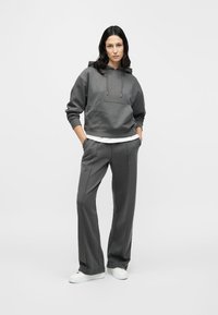 Γκρι φούτερ με κουκούλα και τσέπη μπροστά, συνδυασμένο με γκρι παντελόνι φαρδιάς γραμμής. Άσπρα αθλητικά παπούτσια συμπληρώνουν το casual σύνολο.