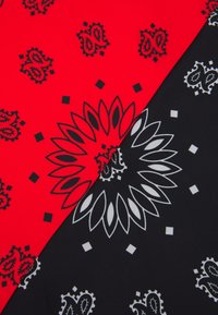 Piros és fekete szövet diagonálisan elválasztva; a piros fekete paisley mintákkal, míg a fekete fehér virágmintával és geometriai díszítésekkel rendelkezik.