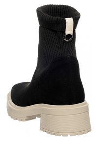 Czarny zamszowy botek za kostkę z prążkowaną dzianinową cholewką, kremową gumową platformą i zawieszką z metalowym pierścieniem z tyłu.