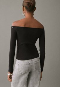 Crna bluzica s dugim rukavima i širokim dekolteom, sa pripijenim krojem, izrađena od rastezljivog materijala; uparena s laganim svijetlosivim trapericama visokog struka.