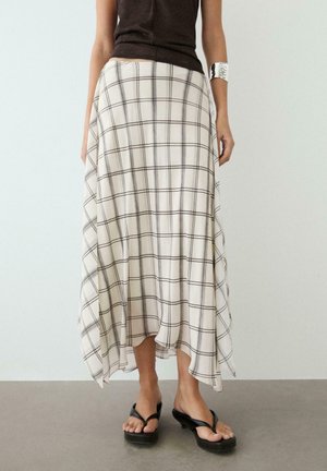 Frau trägt schwarzen ärmellosen Top, weißen knöchellangen Rock mit schwarzem Karomuster, silbernes Manschettenarmband und schwarze Plateausandalen.