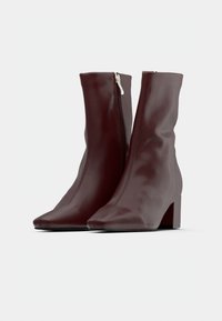 Paire de bottes mi-mollet rouge foncé avec talons carrés et fermetures éclair latérales sur fond blanc uni.