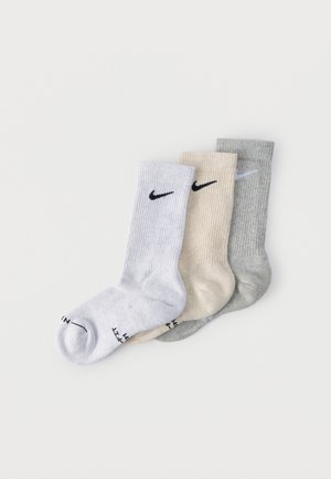 Three ribbed crew socks in white, beige, and gray, each with a small black or white Nike swoosh logo near the top.