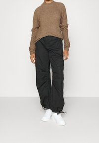 Brun randig stickad tröja med långa ärmar, kombinerad med svarta cargo-byxor med fickor och elastiska ärmslut, samt vita sneakers.