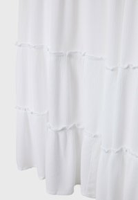 Vit texturerad tyg med draperade sömmar som bildar lager av horisontella volanger på ett flödande plagg eller gardin.