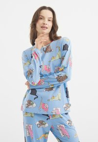 Niebieski komplet pidżamowy z wesołym wzorem kotów. Materiał jest miękki, z długimi rękawami i spodniami. Wzór zawiera różne pozy oraz kolory kotów.