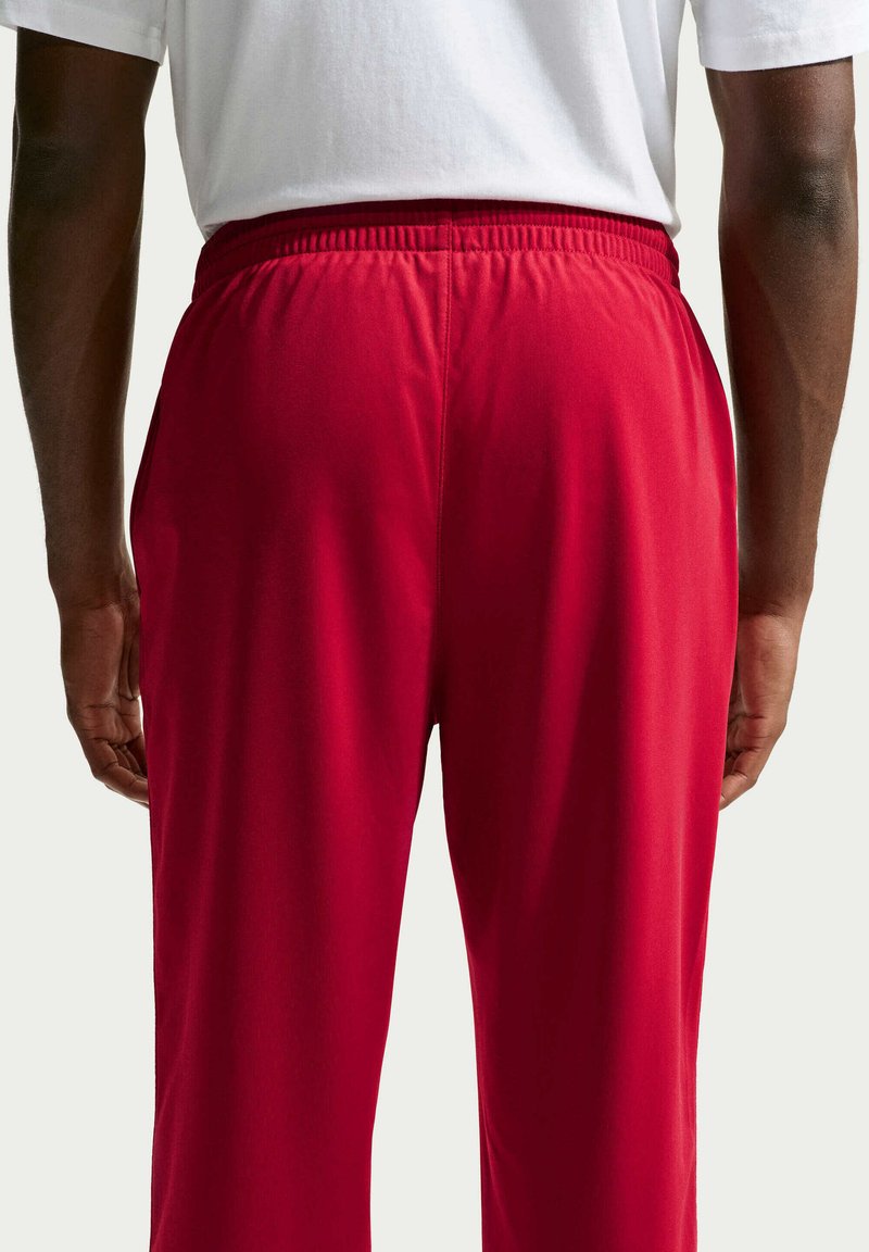 Vista posteriore di una persona che indossa pantaloni rosso acceso con vita elastica e una camicia bianca a maniche corte.