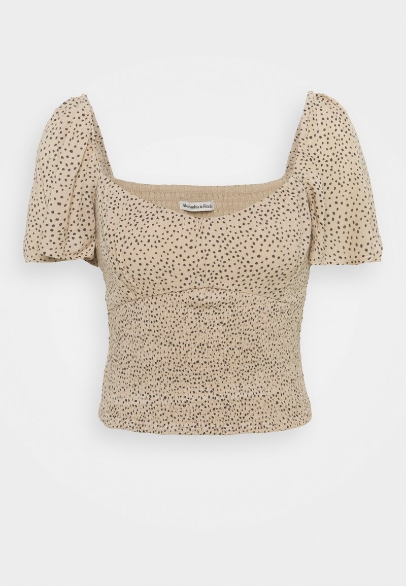 Beige top med korte pufærmer, rynket krop og sort prikkemønster. Firkantet halsudskæring giver struktur. Blødt, tekstureret stof.