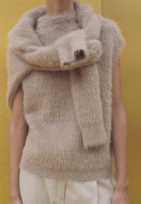 Maglione beige in peluche con un collo alto, caratterizzato da un dettagli a sciarpa drappeggiata. Texture morbida, maniche corte e design stratificato.