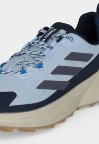 Ανοιχτό μπλε και μαύρο αθλητικό παπούτσι Adidas Terrex με πολύχρωμα κορδόνια και μπεζ υφή στη σόλα, σχεδιασμένο για υπαίθριες δραστηριότητες.