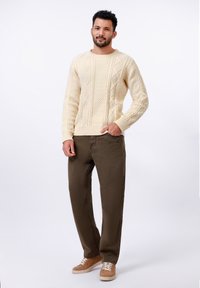 Pull en mailles torsadées crème avec des motifs texturés, associé à un pantalon vert olive et des baskets beiges avec des lacets blancs. Style décontracté.