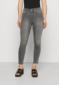 Jeans skinny em denim cinza com uma cintura alta, apresentando bolsos frontais e traseiros e um desbotado sutil. Combinados com sandálias de plataforma pretas tipo slip-on.
